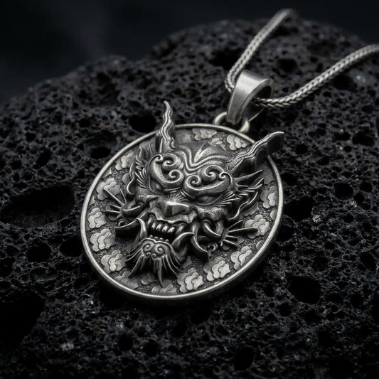 Oxidized sterling silver Japanese Oni mask pendant on black volcanic rock, featuring fierce curved horns, swirling eyebrows, sharp fangs, and traditional Japanese cloud motifs.