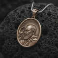 Load image into Gallery viewer, Bronze Padre Pio pendant on black volcanic rock, featuring Saint Pio of Pietrelcina with a raised blessing hand, detailed beard, halo, and traditional Franciscan habit.
