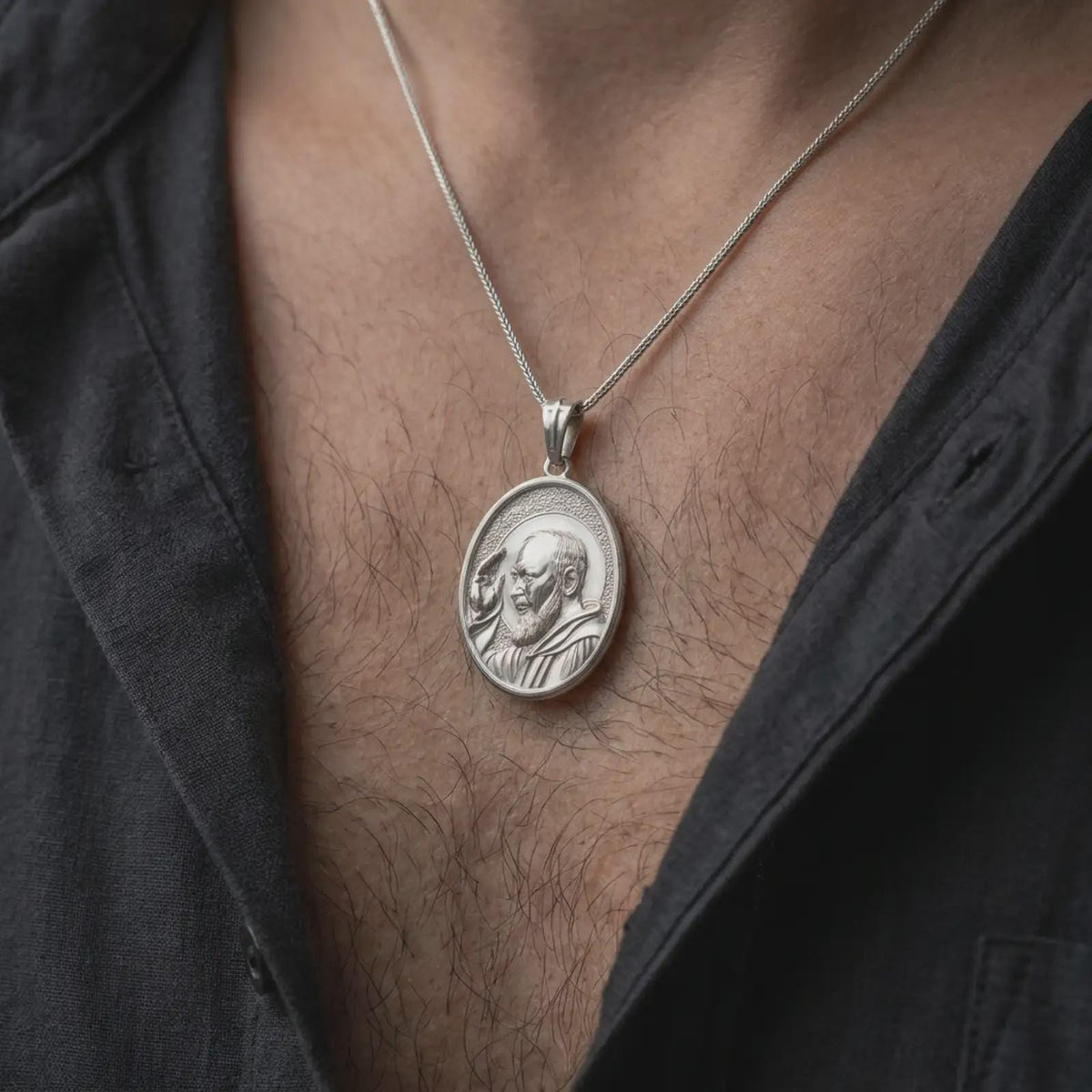 Polished silver Saint Padre Pio pendant worn on the chest, featuring the detailed Franciscan saint portrait, circular halo, traditional religious habit, and elegant oval Catholic medal.