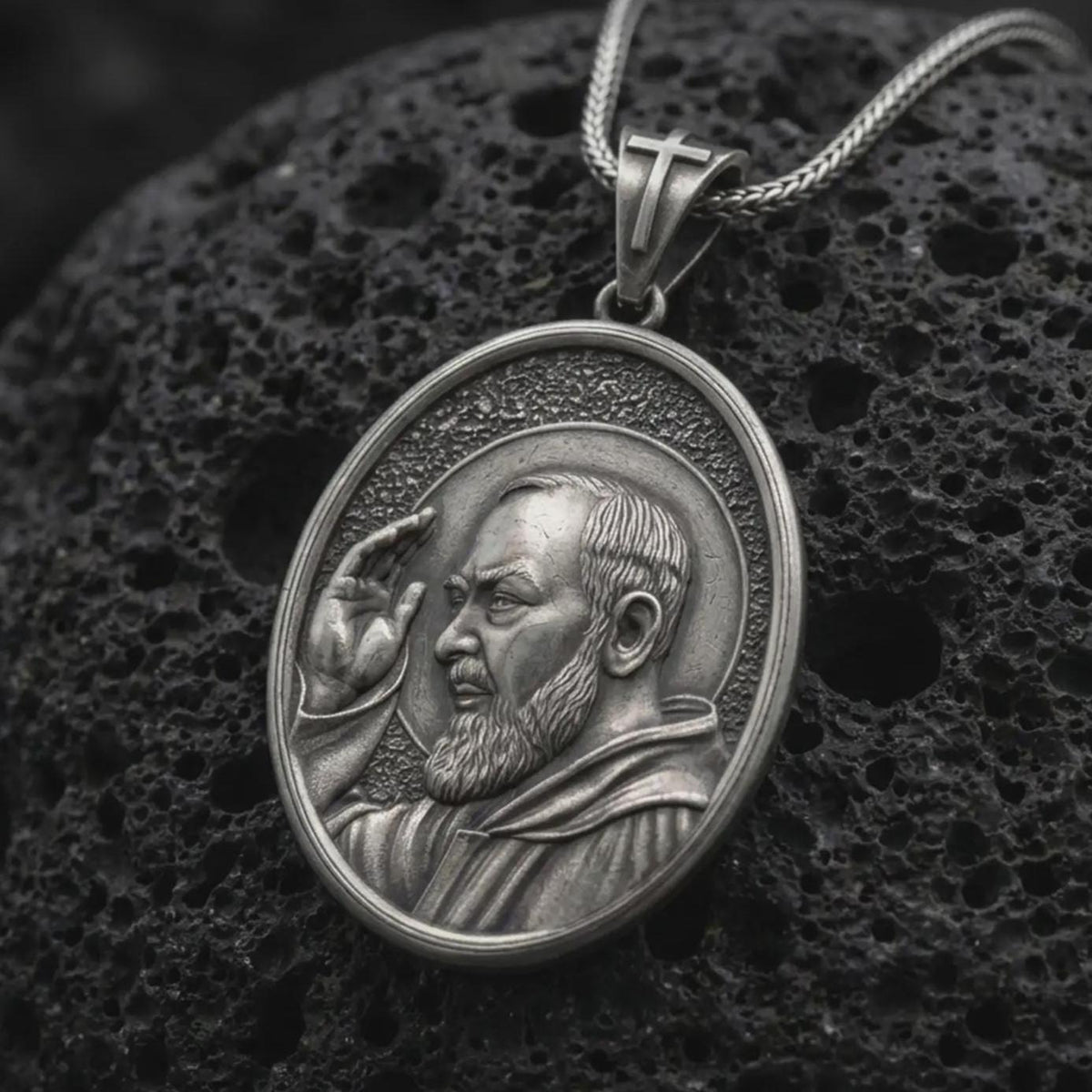 Oxidized sterling silver Padre Pio pendant on black volcanic rock, featuring Saint Pio of Pietrelcina with a raised blessing hand, detailed beard, halo, and traditional Franciscan habit.