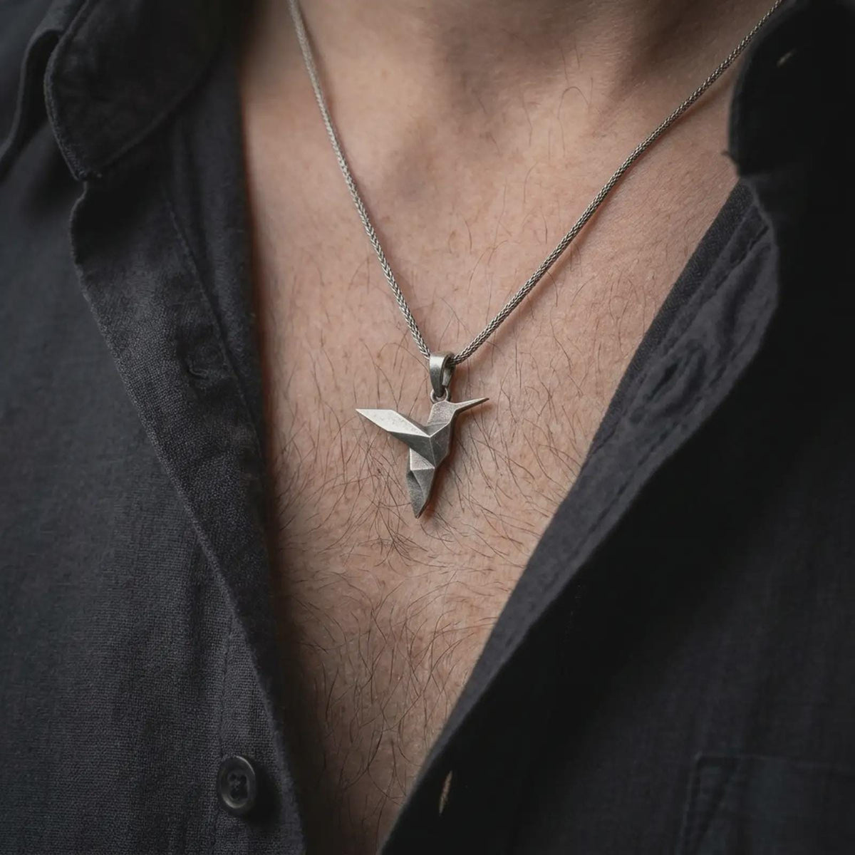 Oxidized sterling silver origami hummingbird necklace worn on the chest, showing the clean geometric bird silhouette, pointed beak, and modern minimalist pendant style.