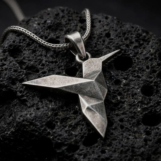 Oxidized sterling silver origami hummingbird pendant on black volcanic rock, featuring a geometric folded bird design with a long pointed beak and angular wings.