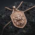 Load image into Gallery viewer, Rose gold plated lion shield necklace displayed on textured volcanic stone, showcasing the dimensional roaring lion head, expressive eyes, open mouth, and intricately sculpted fur details.
