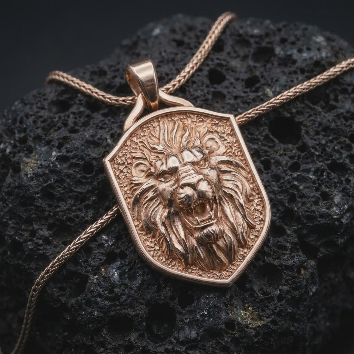 Rose gold plated lion shield necklace displayed on textured volcanic stone, showcasing the dimensional roaring lion head, expressive eyes, open mouth, and intricately sculpted fur details.