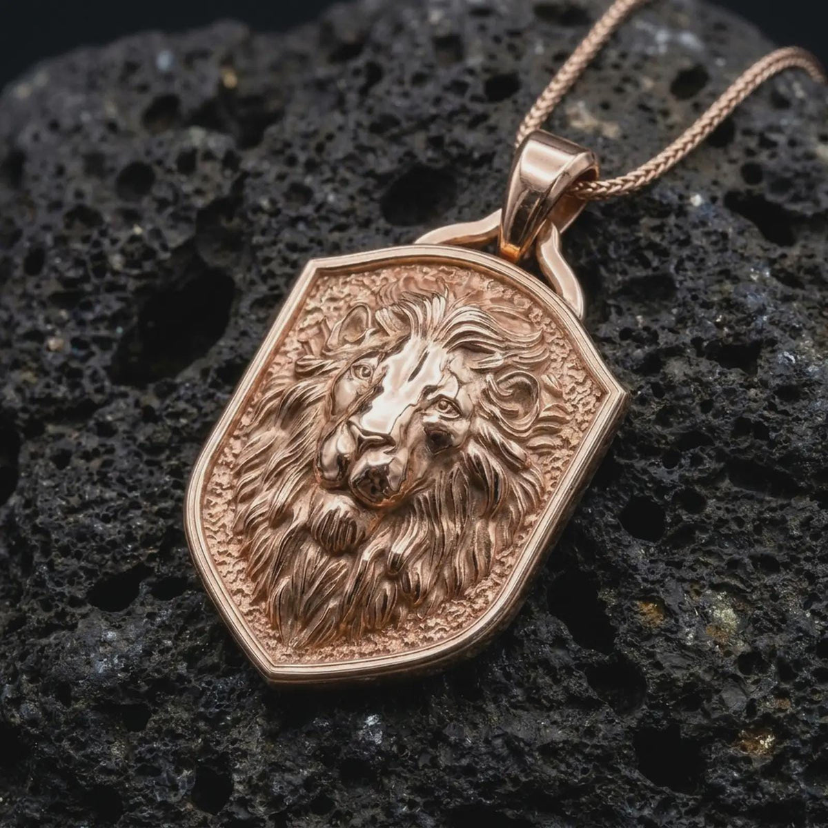 Rose gold plated lion shield necklace displayed on textured volcanic stone, showcasing the dimensional lion portrait, symmetrical facial features, flowing fur details, and elegant wildlife-inspired design.