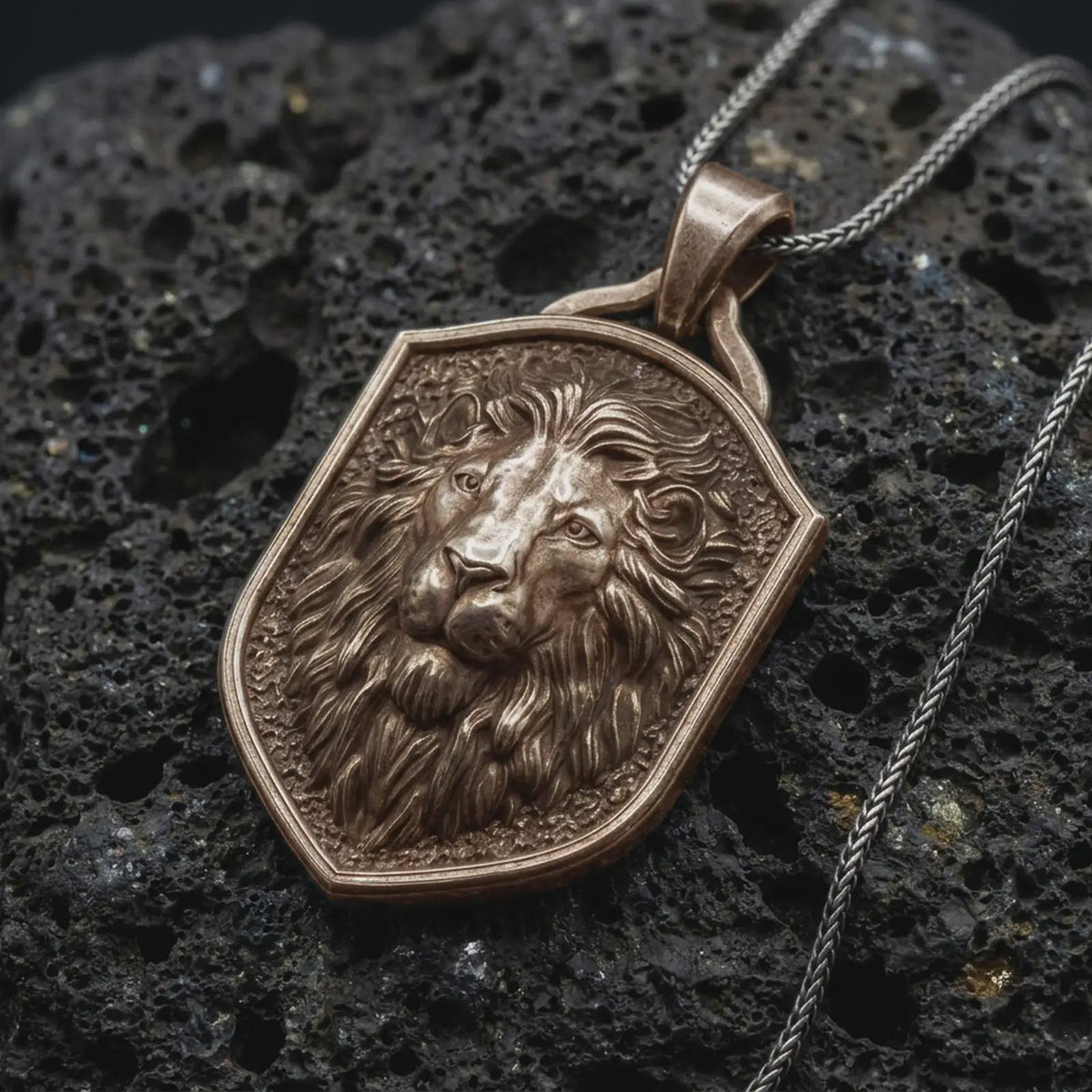 Bronze regal lion shield pendant on black volcanic rock, featuring a majestic lion portrait, calm expression, flowing mane, and textured heraldic shield background.