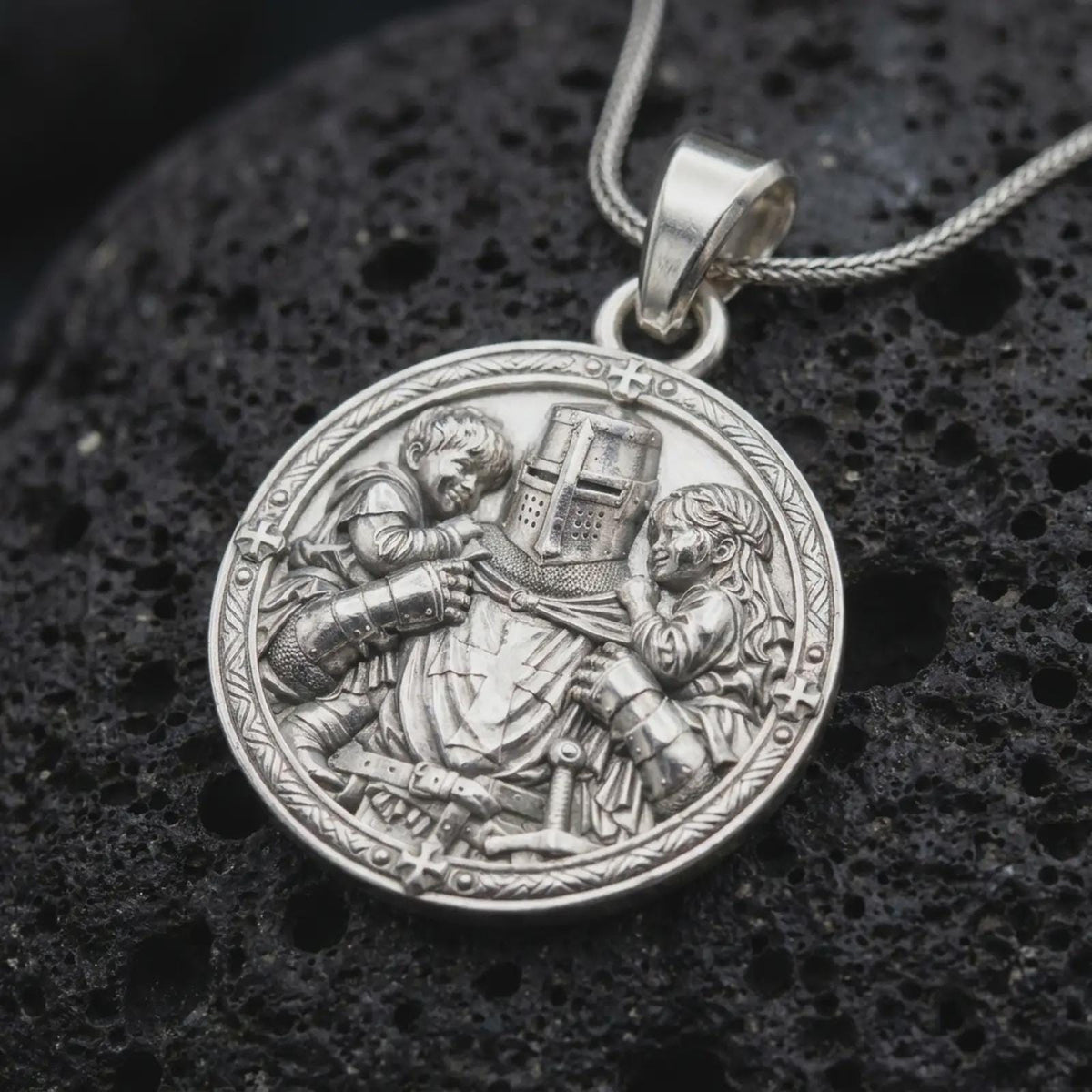 Polished sterling silver guardian knight necklace displayed on dark volcanic stone, highlighting the medieval warrior embracing two children, detailed plate armor, sword, and Christian cross symbols.