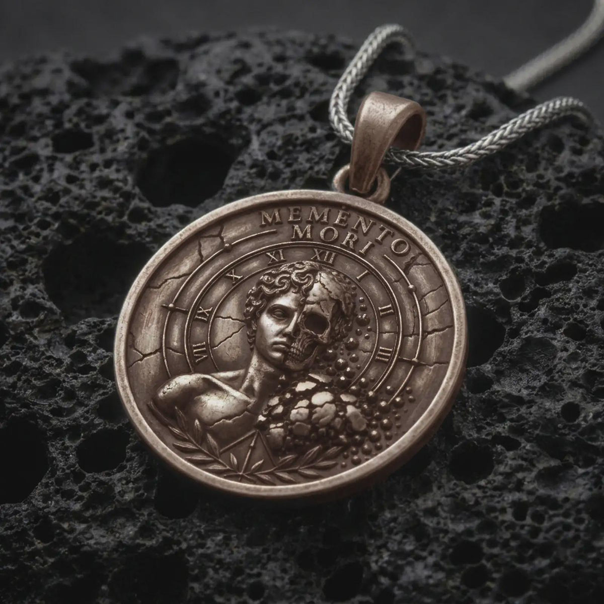 Bronze Memento Mori pendant on black volcanic rock, featuring a half-human half-skull portrait, Roman numeral clock markings, cracked stone details, and engraved Memento Mori lettering.