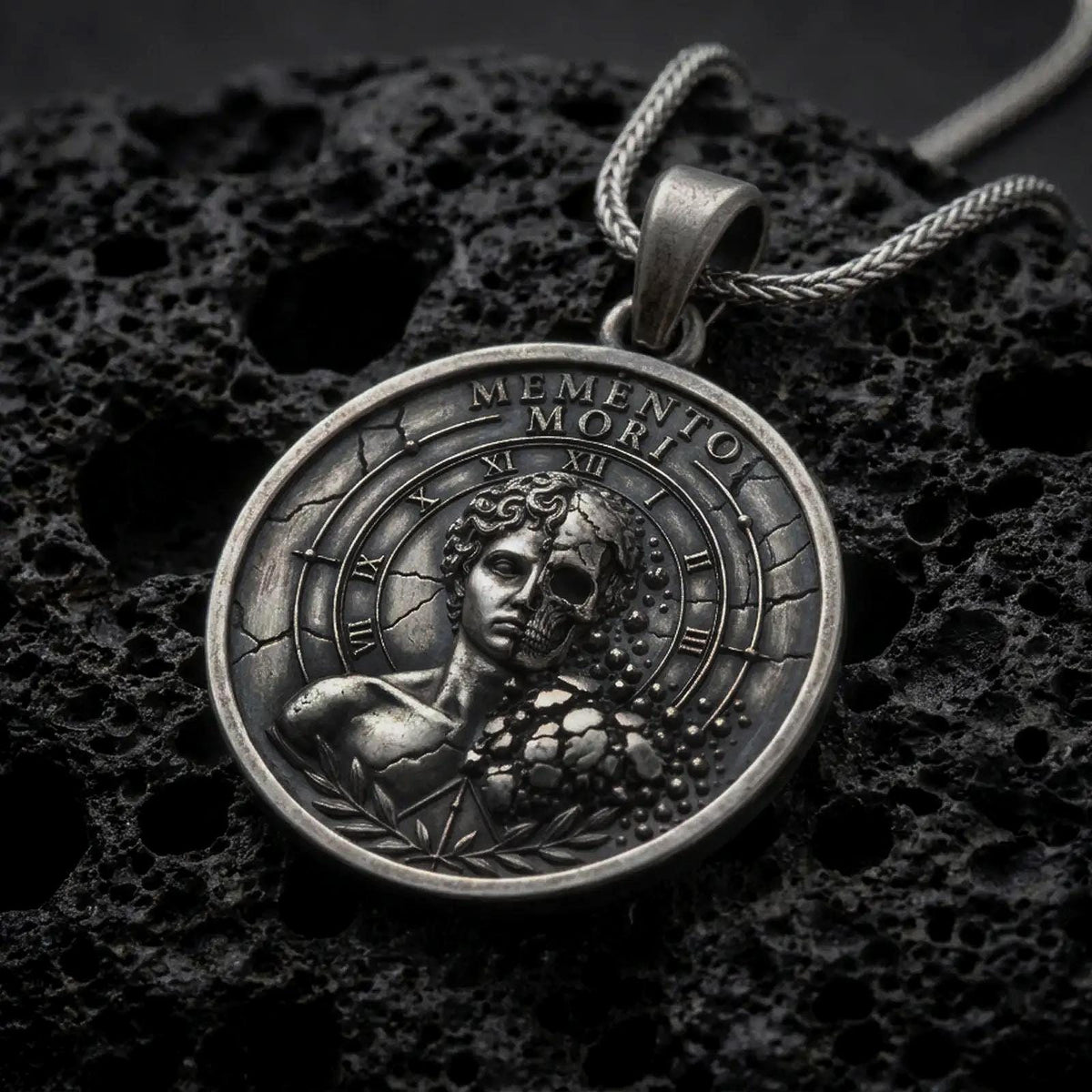 Oxidized sterling silver Memento Mori pendant on black volcanic rock, featuring a half-human half-skull portrait, Roman numeral clock markings, cracked stone details, and engraved Memento Mori lettering.