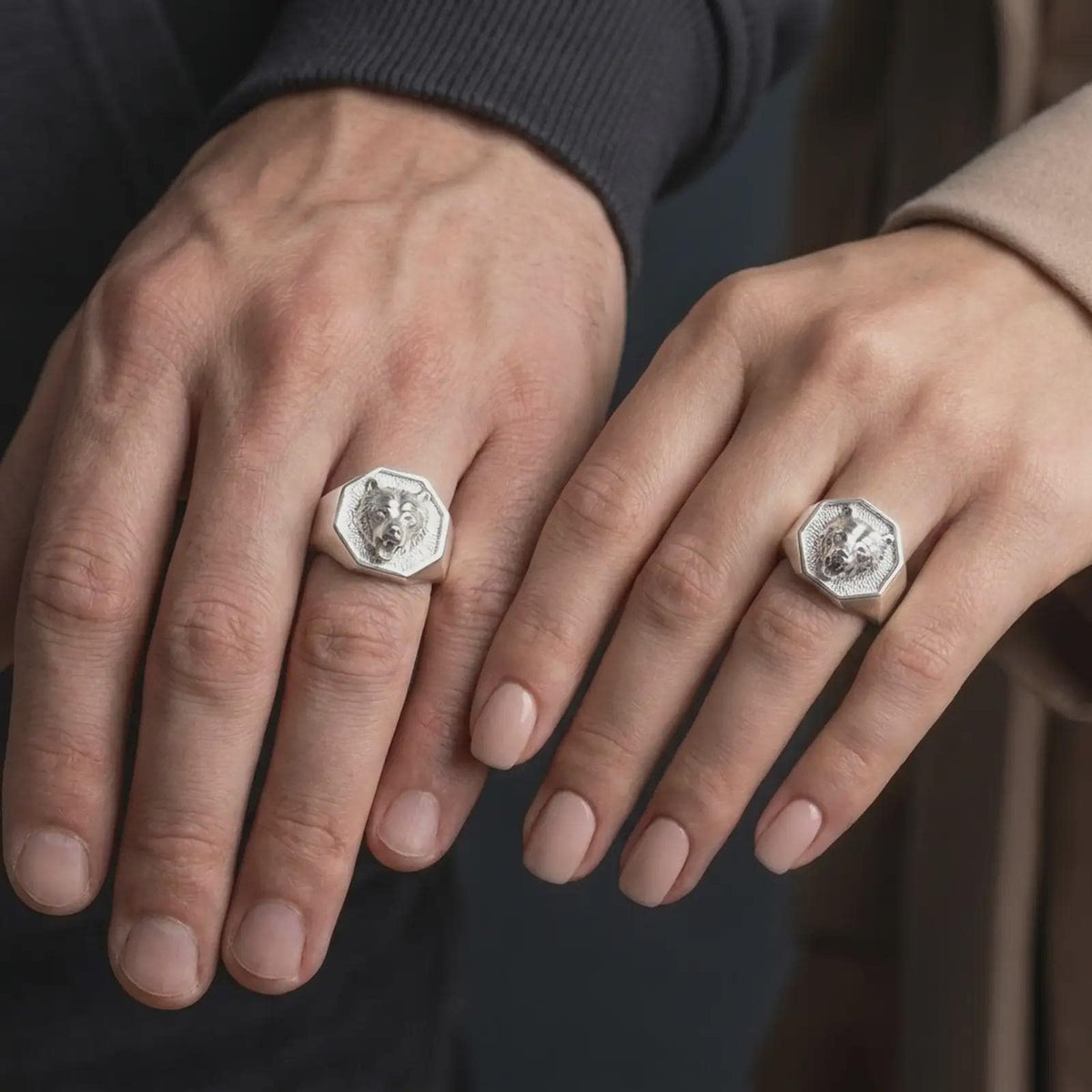 Polished 925 sterling silver matching bear head rings worn on the fingers of a man and woman together, showcasing roaring bear sculptures, detailed canine teeth, textured hexagonal signet faces, and bright polished silver finishes.