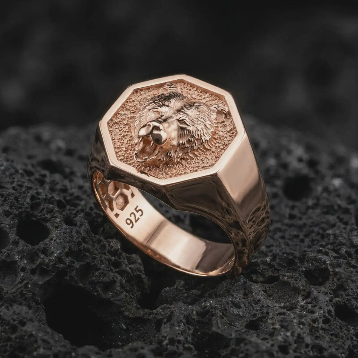Rose gold plated 925 sterling silver bear signet ring resting on black volcanic stone, highlighting the roaring bear portrait, sharp teeth, textured recessed background, broad ring shoulders, and warm rose gold plated finish.