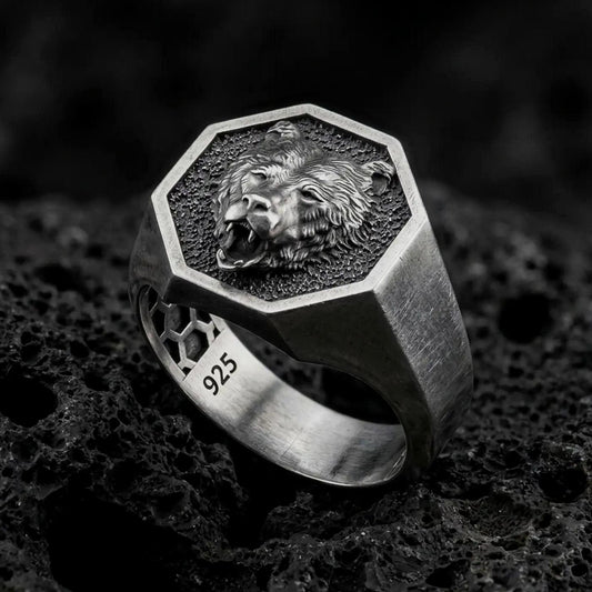 Oxidized 925 sterling silver roaring bear signet ring displayed on textured black volcanic rock, featuring an open-mouthed bear head, sharp fangs, detailed fur, hexagonal frame, and dark oxidized silver finish.
