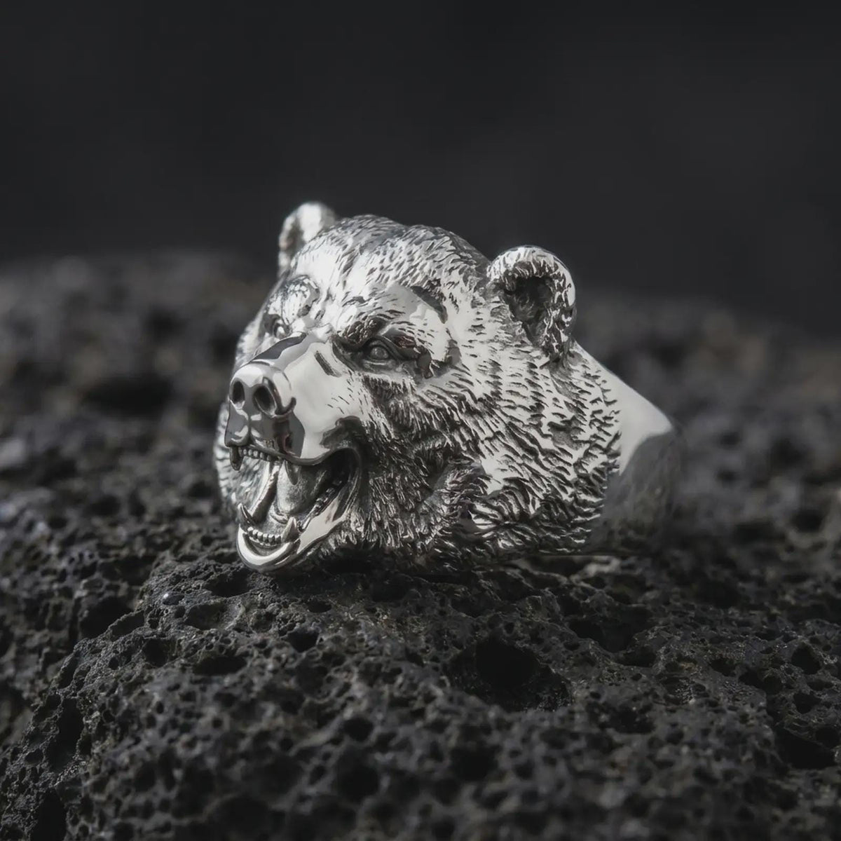 Polished 925 sterling silver 3D bear ring resting on black volcanic stone, showcasing a fierce roaring bear head with lifelike facial features, sculpted fur, prominent canine teeth, powerful jaws, and bright polished silver finish.