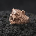 Load image into Gallery viewer, Rose gold plated 925 sterling silver bear head statement ring resting on black volcanic stone, highlighting the realistic bear sculpture, exposed fangs, detailed muzzle, raised fur textures, powerful facial expression, and warm rose gold plated finish.
