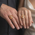 Load image into Gallery viewer, Rose gold plated 925 sterling silver matching eagle head statement rings worn on the fingers of a man and woman together, highlighting fierce bird of prey sculptures, open hooked beaks, layered feather textures, prominent talons, and coordinated rose gold plated finishes.
