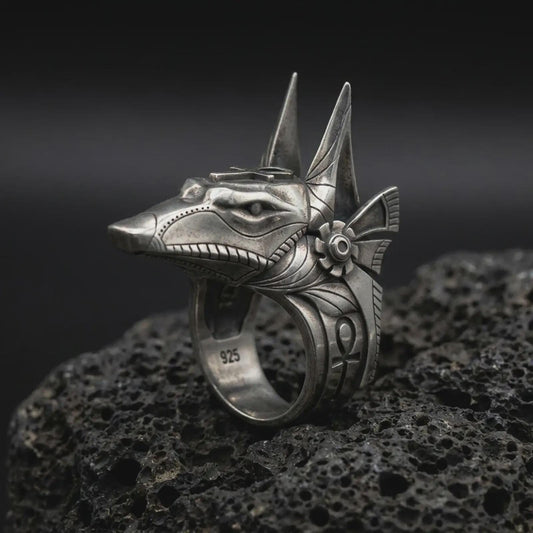 Oxidized 925 sterling silver Anubis ring displayed on textured black volcanic rock, featuring a three-dimensional Egyptian jackal head, tall pointed ears, elongated snout, engraved Ankh symbol, and dark oxidized silver finish.