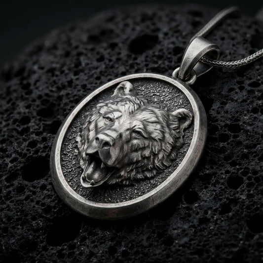 Oxidized 925 sterling silver roaring bear head pendant displayed on textured black volcanic rock, featuring a realistic open-mouthed bear portrait, sculpted fur, exposed teeth, dark recessed oval background, and oxidized silver finish.