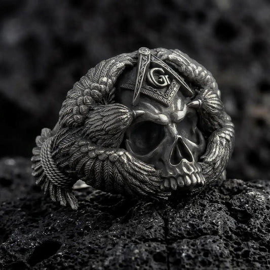Oxidized sterling silver Masonic skull ring on black volcanic rock, featuring a detailed skull, Freemason Square and Compasses emblem with the letter G, and intricately sculpted eagle wings.