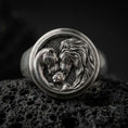 Load image into Gallery viewer, Oxidized sterling silver lion family signet ring on black volcanic rock, featuring a majestic male lion, protective lioness, and their cub nestled together inside a circular medallion.
