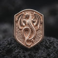 Load image into Gallery viewer, Rose gold plated medieval dragon signet ring displayed on textured volcanic stone, showcasing the raised dragon figure, detailed reptilian scales, extended wings, and distinctive shield-shaped signet face.
