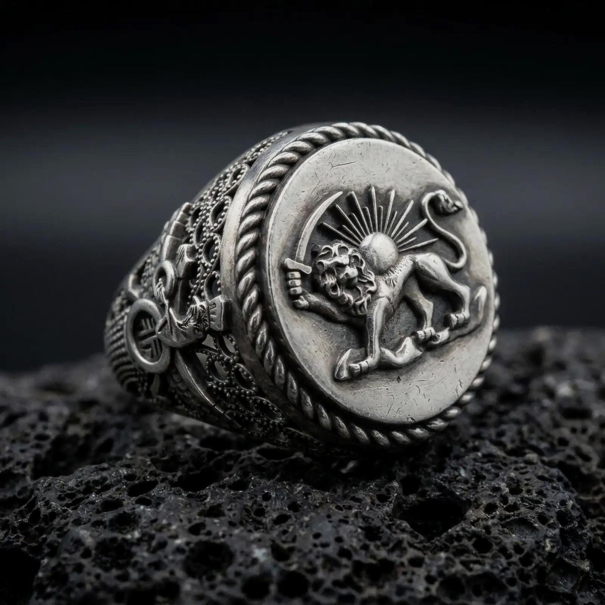 Oxidized sterling silver Persian Lion and Sun signet ring on black volcanic rock, featuring the historic Shir o Khorshid emblem, sword-bearing lion, radiant sun, and twisted rope border.