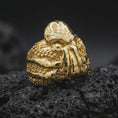 Load image into Gallery viewer, Gold plated Cthulhu octopus ring resting on black volcanic rock, featuring a three-dimensional eldritch horror creature with a ridged head, hanging facial tentacles, and detailed suction cup textures along the sides.
