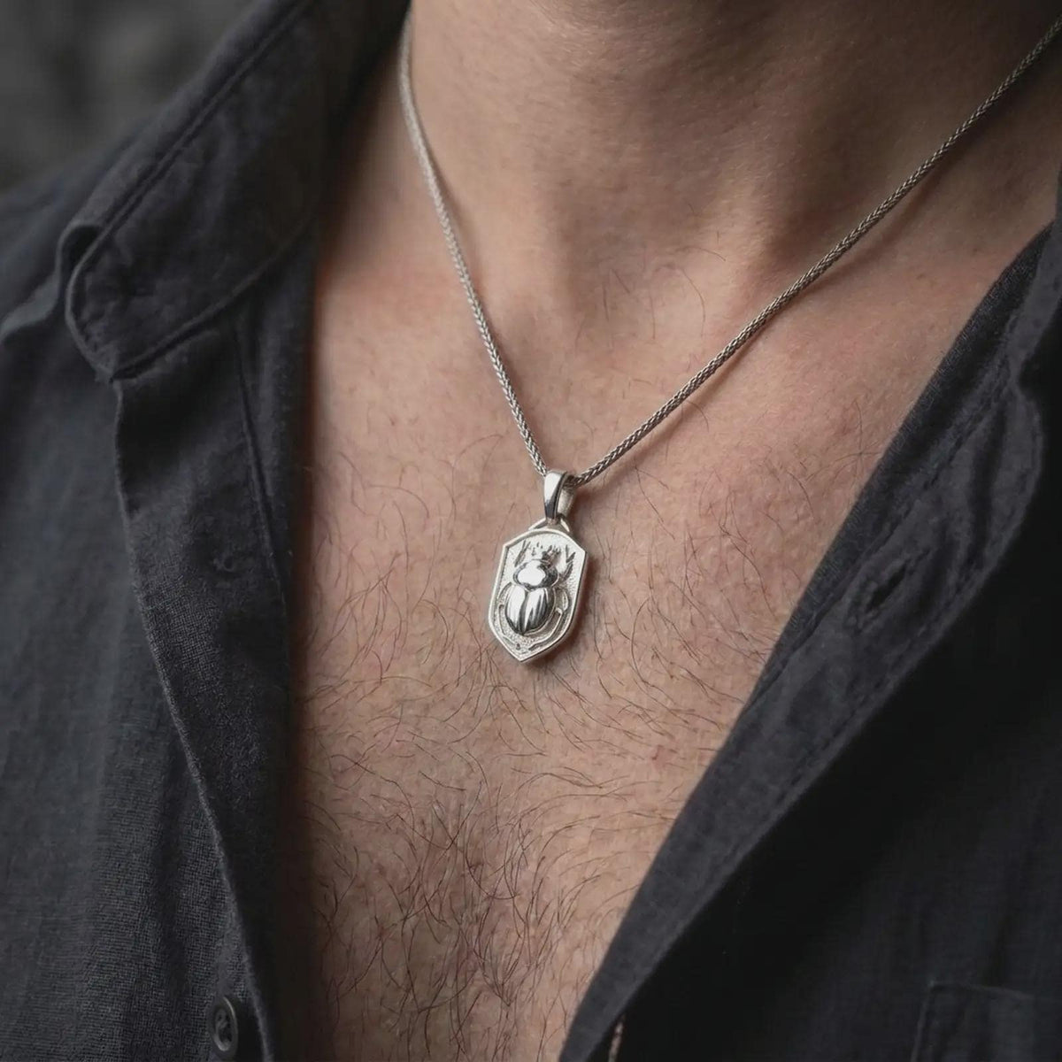 Polished silver stag beetle shield pendant worn on the chest, featuring the sculpted beetle with curved antler-like mandibles, smooth wing covers, textured body, and detailed shield-shaped frame.
