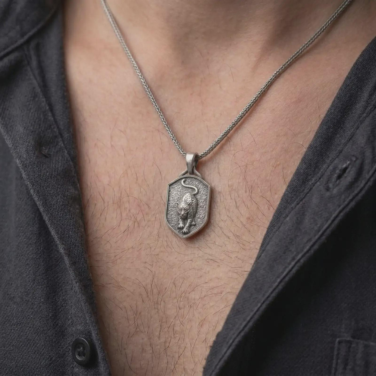 Oxidized sterling silver leopard pendant worn around the neck, showing the prowling wild cat with detailed spots, muscular body, curved tail, dark recessed shield-shaped face, and silver necklace chain.