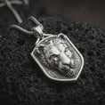 Load image into Gallery viewer, Polished sterling silver lioness pendant displayed on dark volcanic rock, highlighting the sculpted wild cat face, focused eyes, defined ears, smooth muzzle, and bold shield-shaped silver border.

