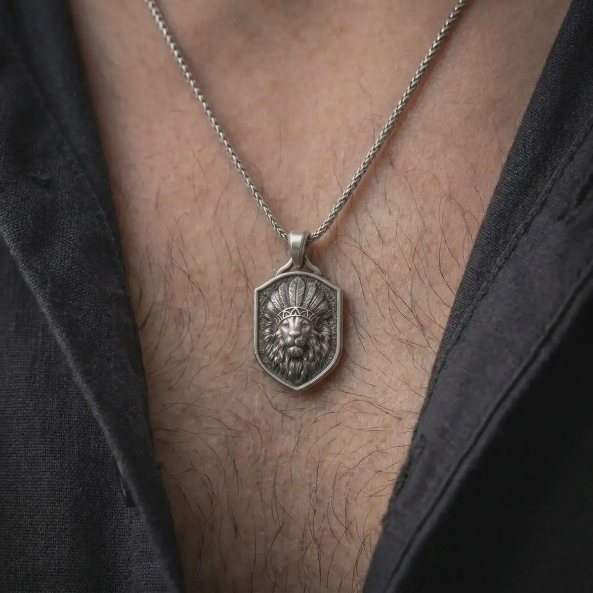 Oxidized sterling silver lion chief necklace worn around the neck, showing the raised lion portrait with a ceremonial-inspired feather headdress, dark textured shield face, flowing mane, and silver chain.