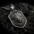Load image into Gallery viewer, Oxidized sterling silver lion chief pendant necklace on black volcanic stone, featuring a majestic lion head wearing a detailed feather headdress, flowing mane, textured shield-shaped background, and braided silver chain.
