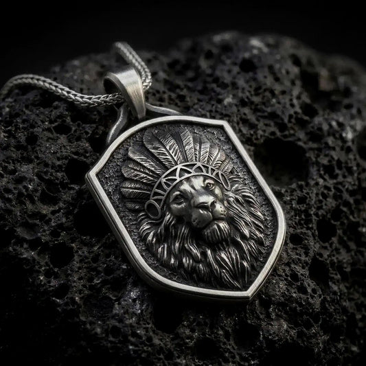 Oxidized sterling silver lion chief pendant necklace on black volcanic stone, featuring a majestic lion head wearing a detailed feather headdress, flowing mane, textured shield-shaped background, and braided silver chain.