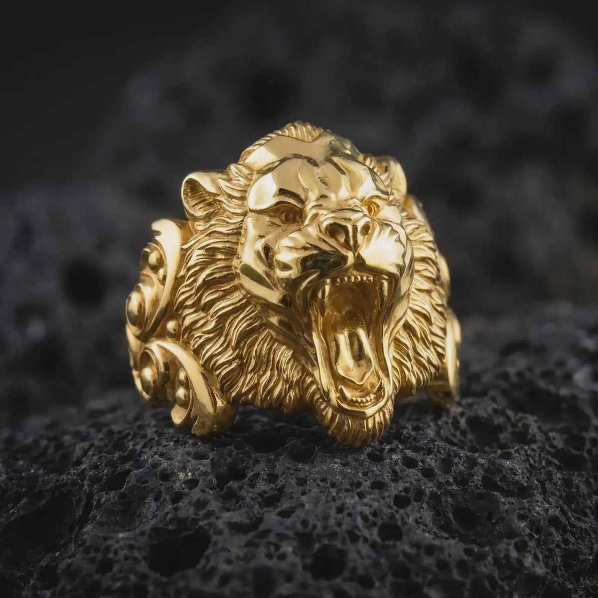 Gold plated roaring tiger ring resting on volcanic stone, highlighting the aggressive big cat face, open jaws, detailed fur strands, and bold masculine animal jewelry design.