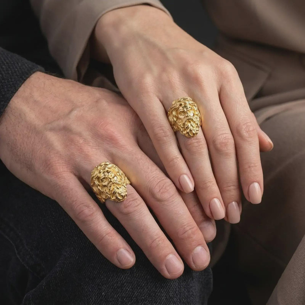 Gold plated sterling silver matching Poseidon rings worn on the fingers of a man and woman together, featuring raised ancient Greek sea god faces, flowing sculpted beards, expressive features, and matching warm gold finishes.
