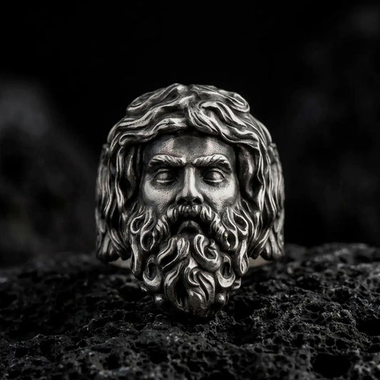 Oxidized 925 sterling silver Poseidon ring displayed on black volcanic rock, featuring a three-dimensional Greek sea god face with flowing wavy hair, deeply sculpted beard, prominent eyebrows, and dark recessed details.