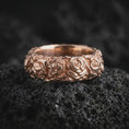 Load image into Gallery viewer, Rose gold plated sterling silver floral band ring resting on black volcanic stone, highlighting continuous sculpted rose blossoms, delicate leaves, dimensional flower petals, and a romantic rose gold finish.
