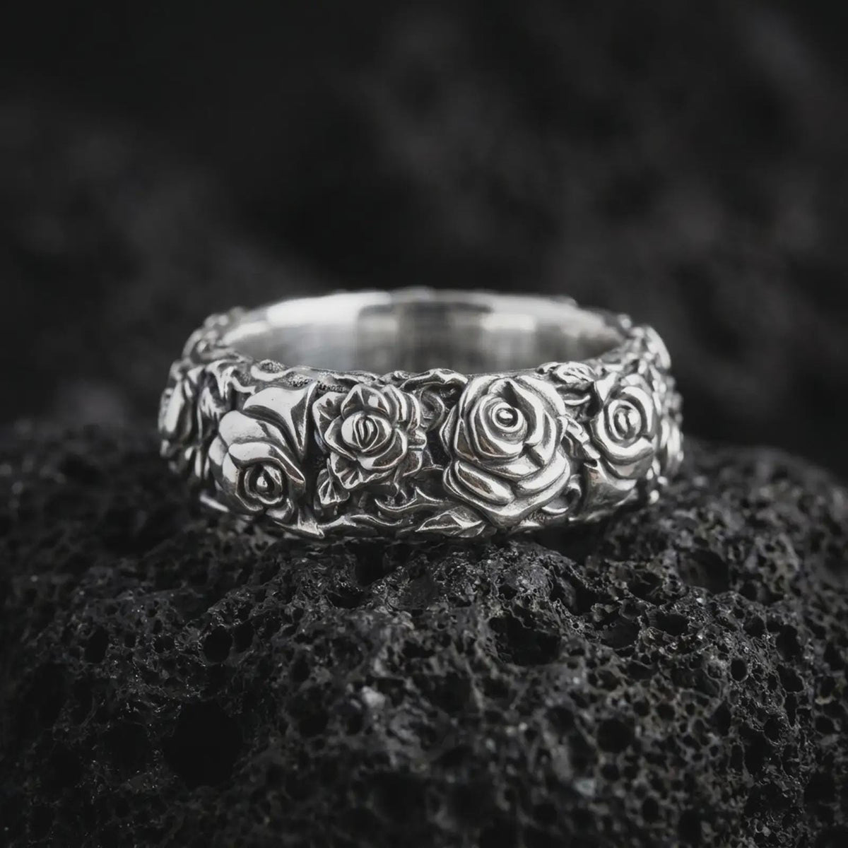 Polished 925 sterling silver rose floral ring resting on black volcanic stone, showcasing raised rose blossoms, intricately sculpted petals, delicate botanical foliage, and a bright polished silver finish.