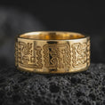 Load image into Gallery viewer, Gold plated 925 sterling silver Aztec Mayan ring displayed on dark volcanic rock, featuring detailed Mesoamerican-inspired pictographs, raised geometric figures, stepped ornamental borders, and a warm polished gold finish.

