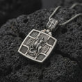 Load image into Gallery viewer, Oxidized Silver Saint George Slaying Dragon pendant on black volcanic rock, featuring the warrior saint on horseback with a spear.
