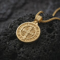 Load image into Gallery viewer, Gold Plated double sided Saint Benedict pendant displayed on black volcanic rock, highlighting the Saint Benedict medal side and cross-decorated bail.
