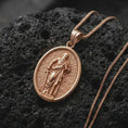 Load image into Gallery viewer, Rose Gold Plated Saint Paul Catholic medal resting on black volcanic rock, featuring the bearded apostle with his traditional book and sword.

