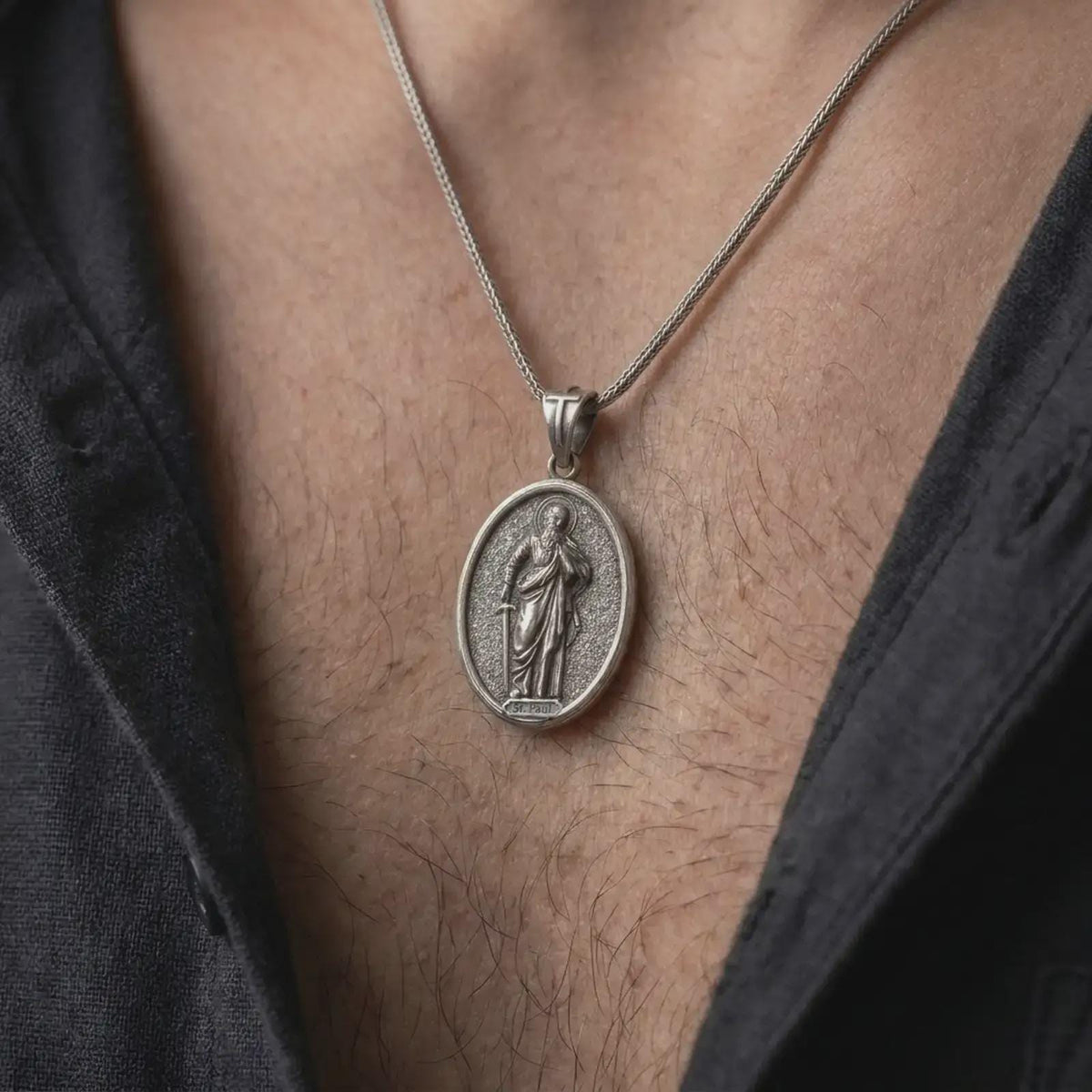 Oxidized Silver Saint Paul Apostle pendant worn on a man's chest with an open black shirt, showcasing the detailed sword and book symbolism.