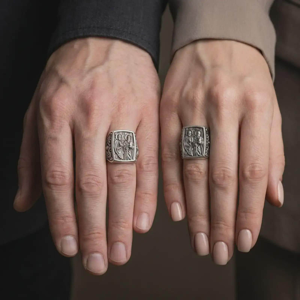 Oxidized Silver Saint Peter and Paul rings worn on the fingers of a man and woman together, showcasing the detailed apostle relief and antique finish.