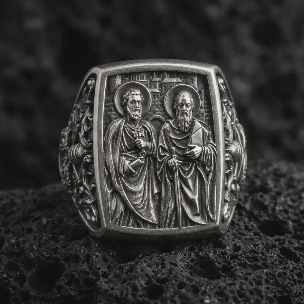 Oxidized Silver Saint Peter and Paul signet ring on black volcanic rock, featuring both haloed apostles with detailed keys, sword, and book symbolism.