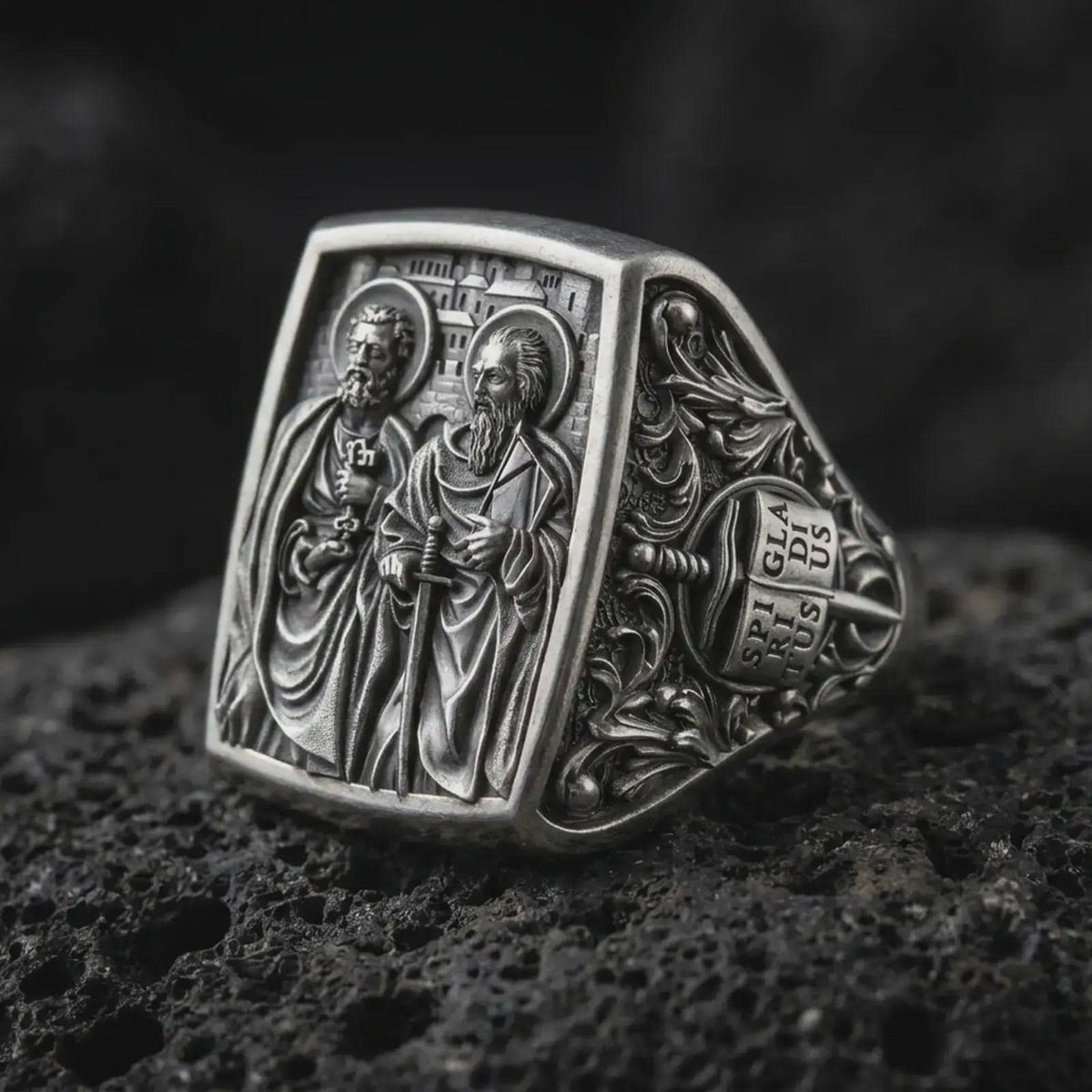 Oxidized Silver Saint Peter and Paul signet ring on black volcanic rock, featuring both haloed apostles with detailed keys, sword, and book symbolism.