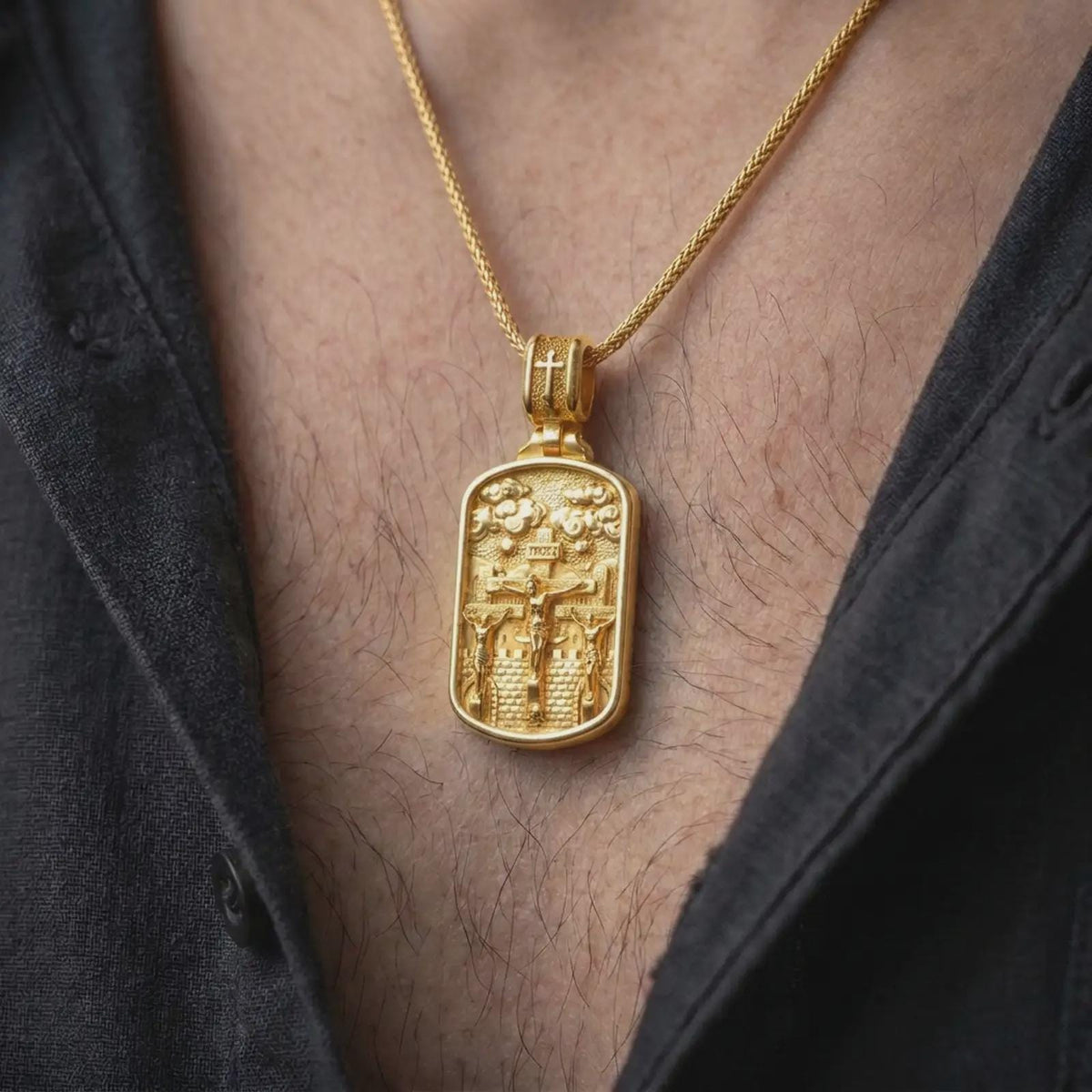 Gold Plated Golgotha Crucifixion pendant worn on a man's chest with an open black shirt, displaying the sculpted Jesus Christ and two thieves.