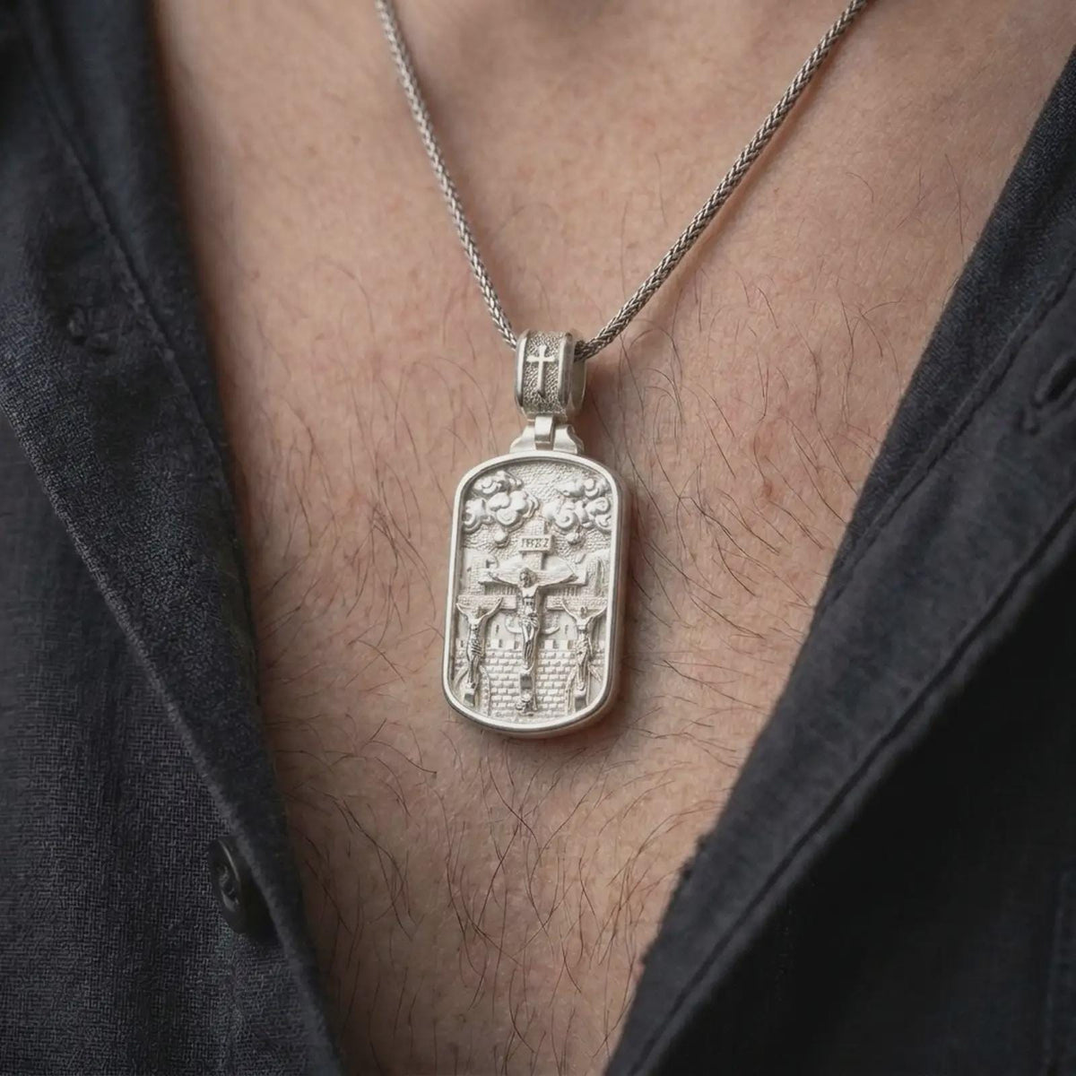Polished Silver Calvary necklace hanging on a man's chest, highlighting the detailed three-cross biblical scene and rectangular medal.