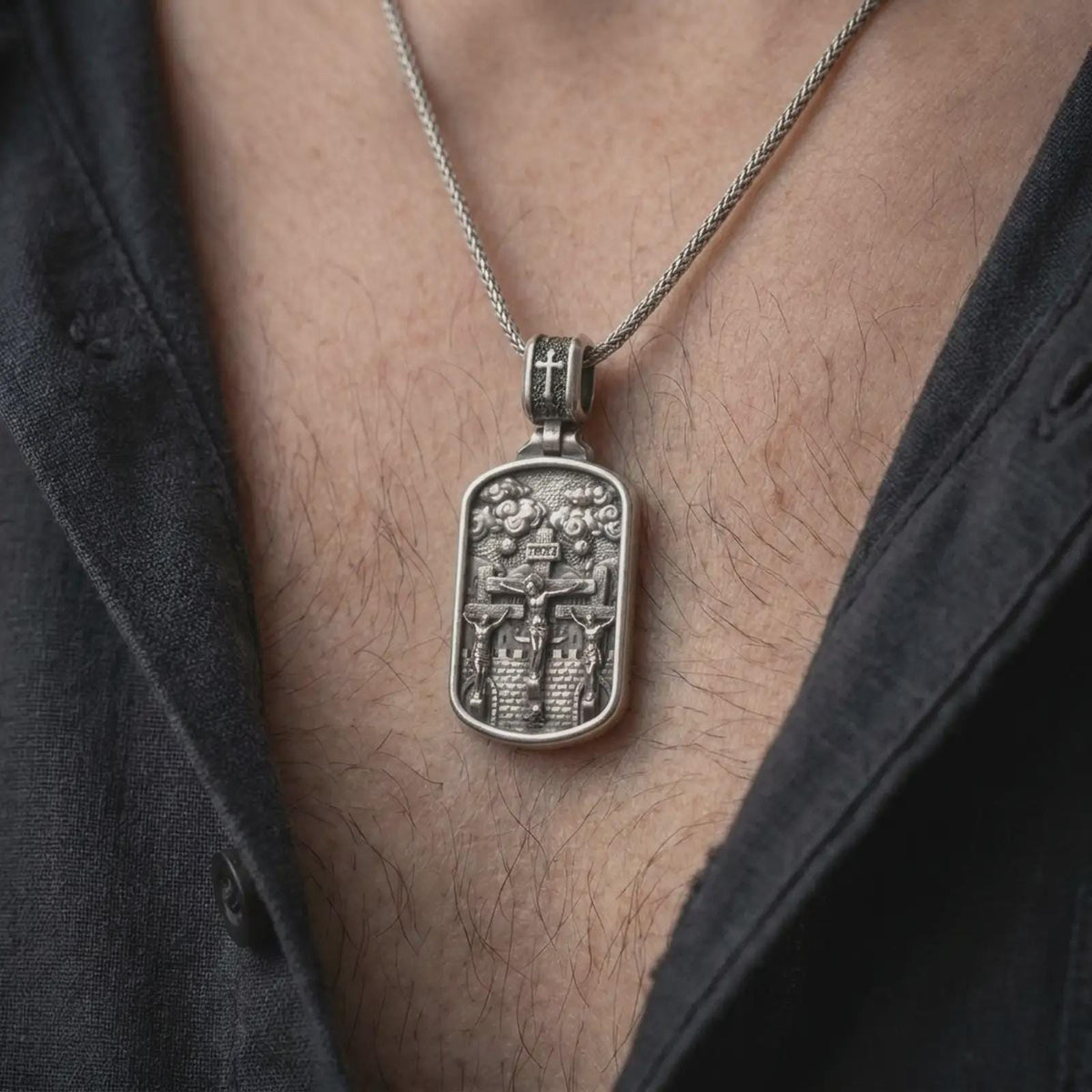 Oxidized Silver Three Crosses Crucifixion pendant worn on a man's chest with an open black shirt, showcasing Jesus between two crucified thieves.