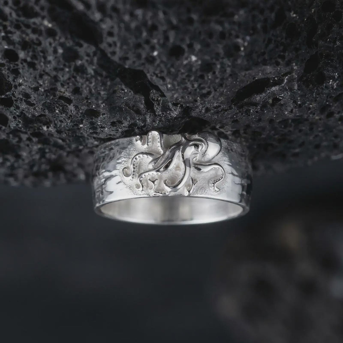 Polished 925 sterling silver octopus ring displayed against black volcanic stone, showcasing a three-dimensional octopus with intertwined tentacles, detailed suction cups, rounded head, smooth wide band, and bright polished silver finish.