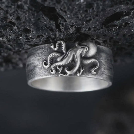 Oxidized 925 sterling silver octopus tentacle ring displayed against textured black volcanic rock, featuring a sculpted octopus with curling arms, raised suction cups, flowing tentacles, wide band design, and dark oxidized silver finish.